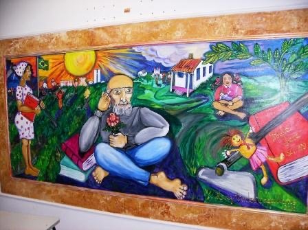 Mural of Paulo Freire in a landscape with sunrise, books, and figures of learners