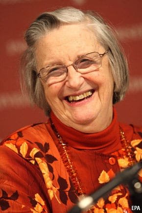 Elinor Ostrom laughing at a podium, wearing an orange floral top